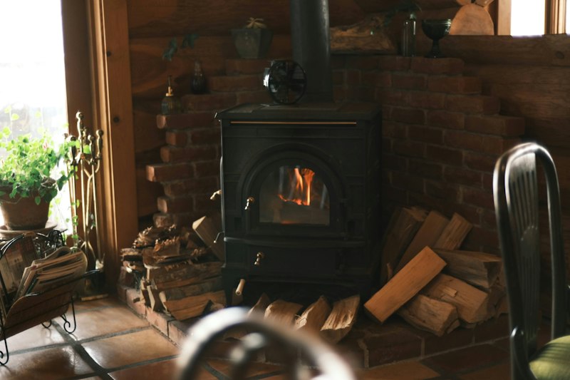 A lit wood stove with split firewood stacked beside it